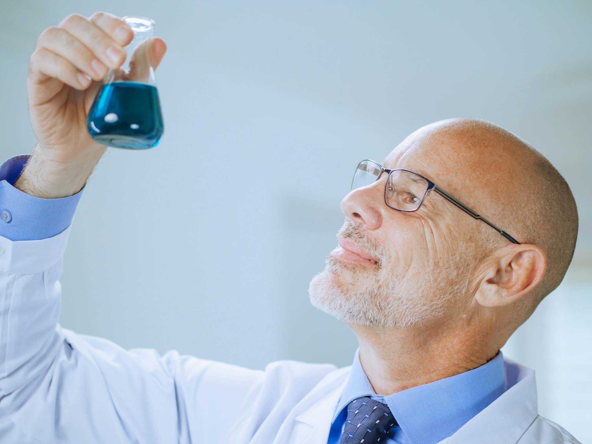 Male scientist examining blue liquid in a lab flask. Science and research concept.